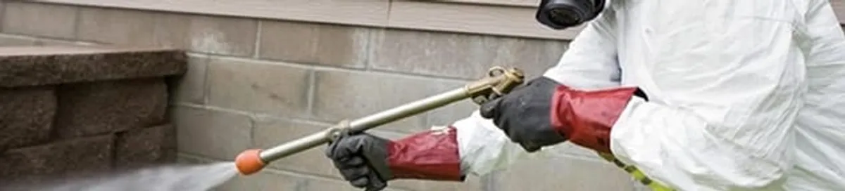 Pest control technician applying exterior insect treatment along a home foundation in Cincinnati, OH