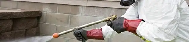 Pest control technician applying exterior insect treatment along a home foundation in Cincinnati, OH