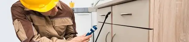 Roach exterminator applying treatment under kitchen cabinets in Cincinnati, OH