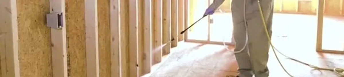 Termite treatment technician applying spray along framing and unfinished walls in Cincinnati, OH