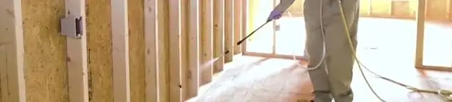 Termite treatment technician applying spray along framing and unfinished walls in Cincinnati, OH